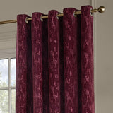 Aurelio Chenille Jacquard eyelet curtains in burgundy, showing textured fabric folds hung on a brass pole with eyelet rings against a neutral wall.