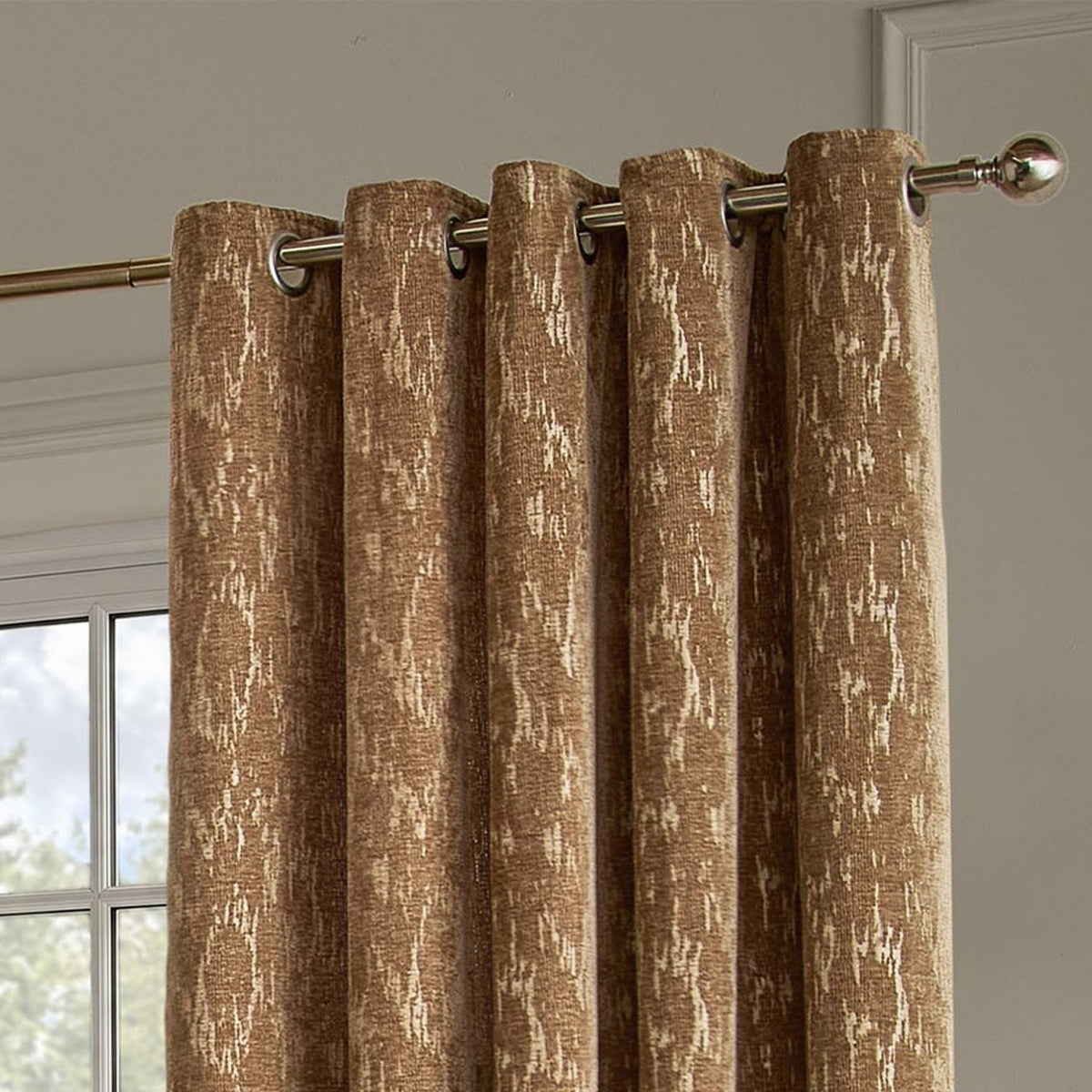 Aurelio Chenille Jacquard Eyelet Curtains in caramel, fully lined with a mottled gold-toned abstract pattern, hung on a chrome pole in a living room setting.