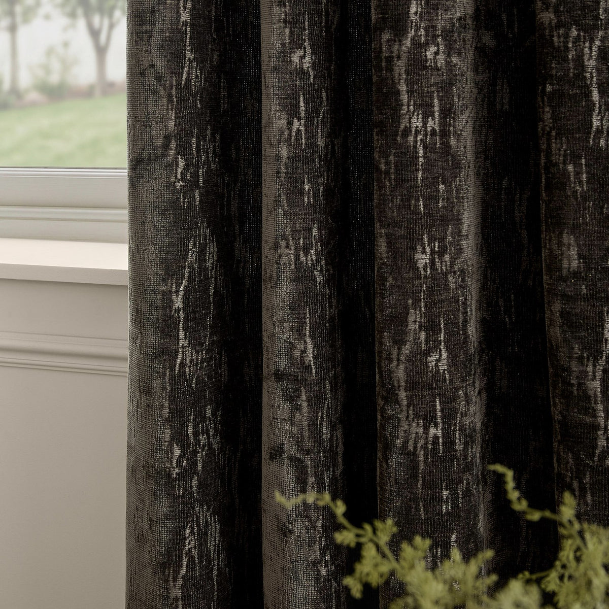 Aurelio Chenille Jacquard Eyelet Curtains in charcoal, showing textured abstract jacquard weave with pale flecks, hung beside a window in a living room setting.