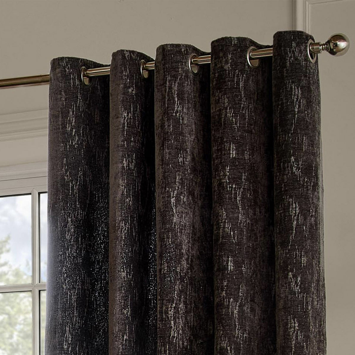 Aurelio Chenille Jacquard fully lined eyelet curtains in charcoal, showing metal eyelet rings on a chrome pole against a light-coloured wall near a window.