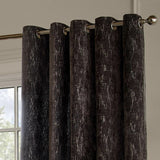 Aurelio Chenille Jacquard fully lined eyelet curtains in charcoal, showing metal eyelet rings on a chrome pole against a light-coloured wall near a window.