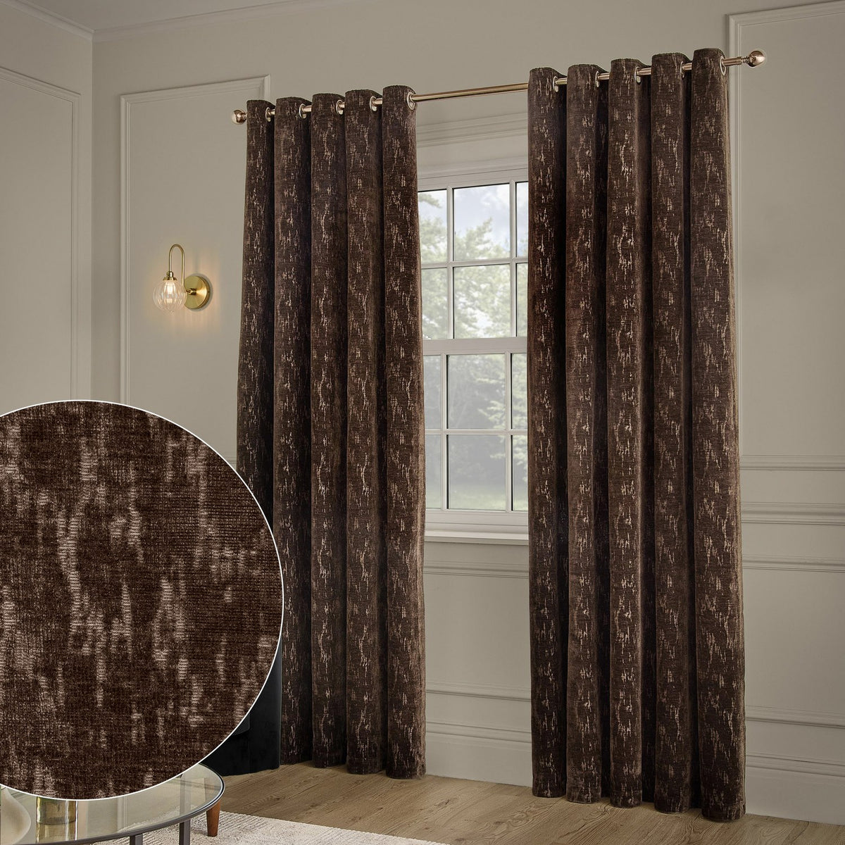Aurelio Chenille Jacquard Fully Lined Eyelet Curtains in chocolate brown with a subtle abstract pattern, shown hanging on a rod beside a window in a neutral-toned living room.