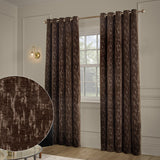 Aurelio Chenille Jacquard Fully Lined Eyelet Curtains in chocolate brown with a subtle abstract pattern, shown hanging on a rod beside a window in a neutral-toned living room.