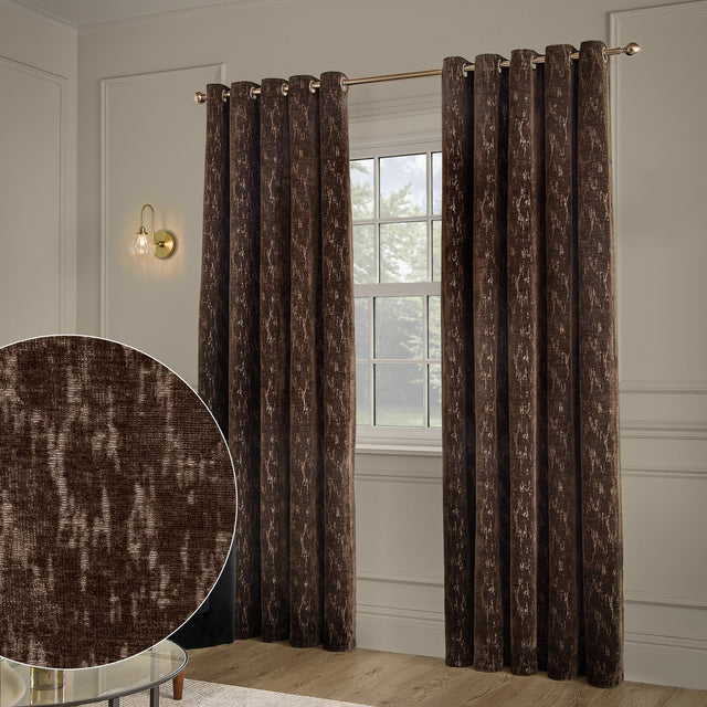 Aurelio Chenille Jacquard Fully Lined Eyelet Curtains in chocolate brown with a subtle abstract pattern, shown hanging on a rod beside a window in a neutral-toned living room.