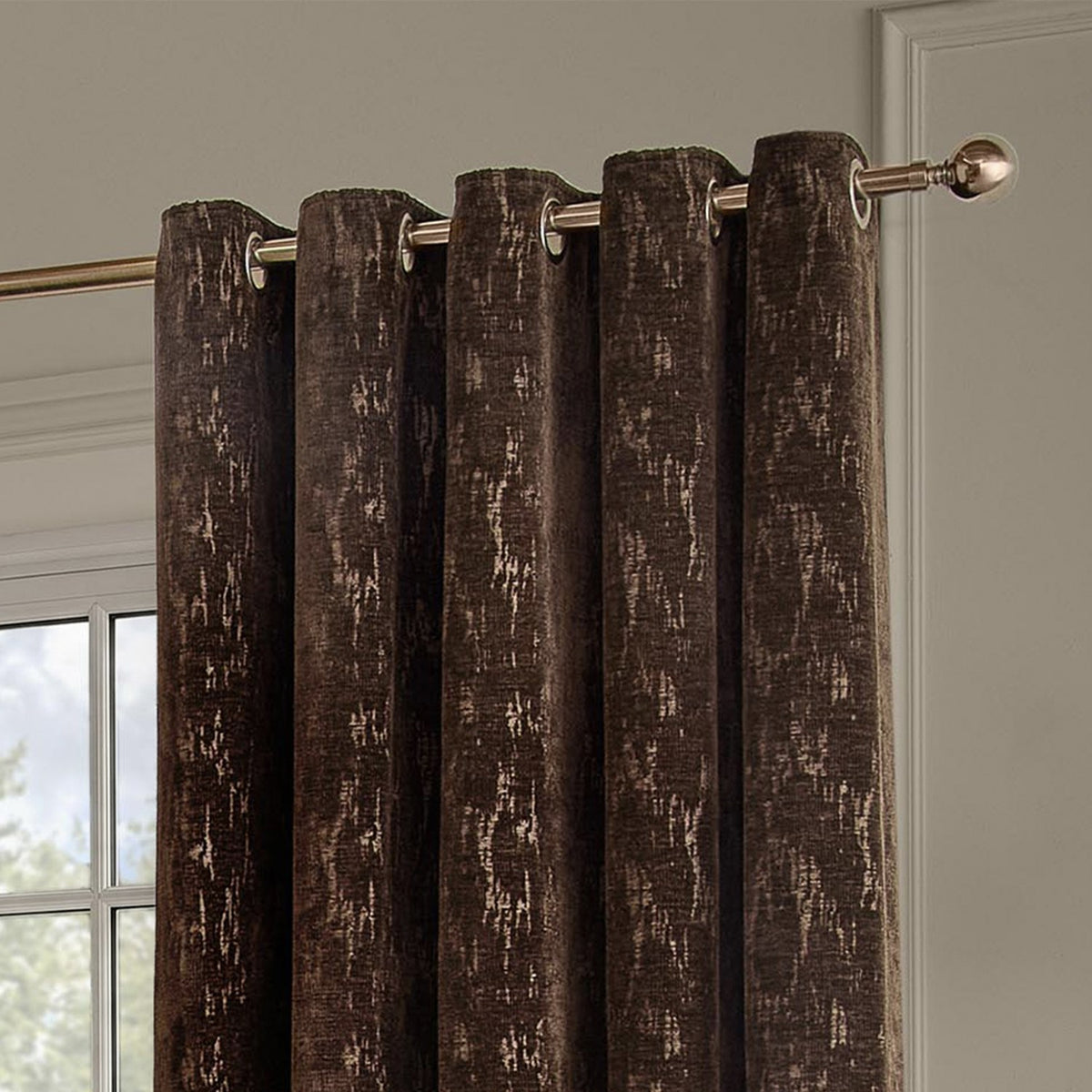 Aurelio Chenille Jacquard Eyelet Curtains in chocolate brown, fully lined with an abstract woven pattern, shown hanging on a bronze-tone pole in a room setting.