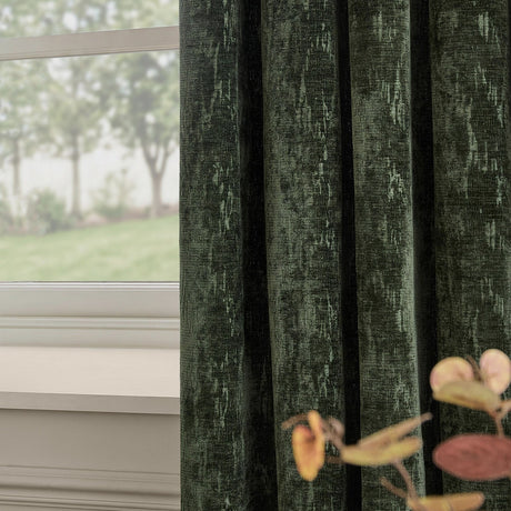 Aurelio Chenille Jacquard Eyelet Curtains in emerald, hung in folds by a window, showing the fabric's textured weave and subtle sheen against a soft interior setting.