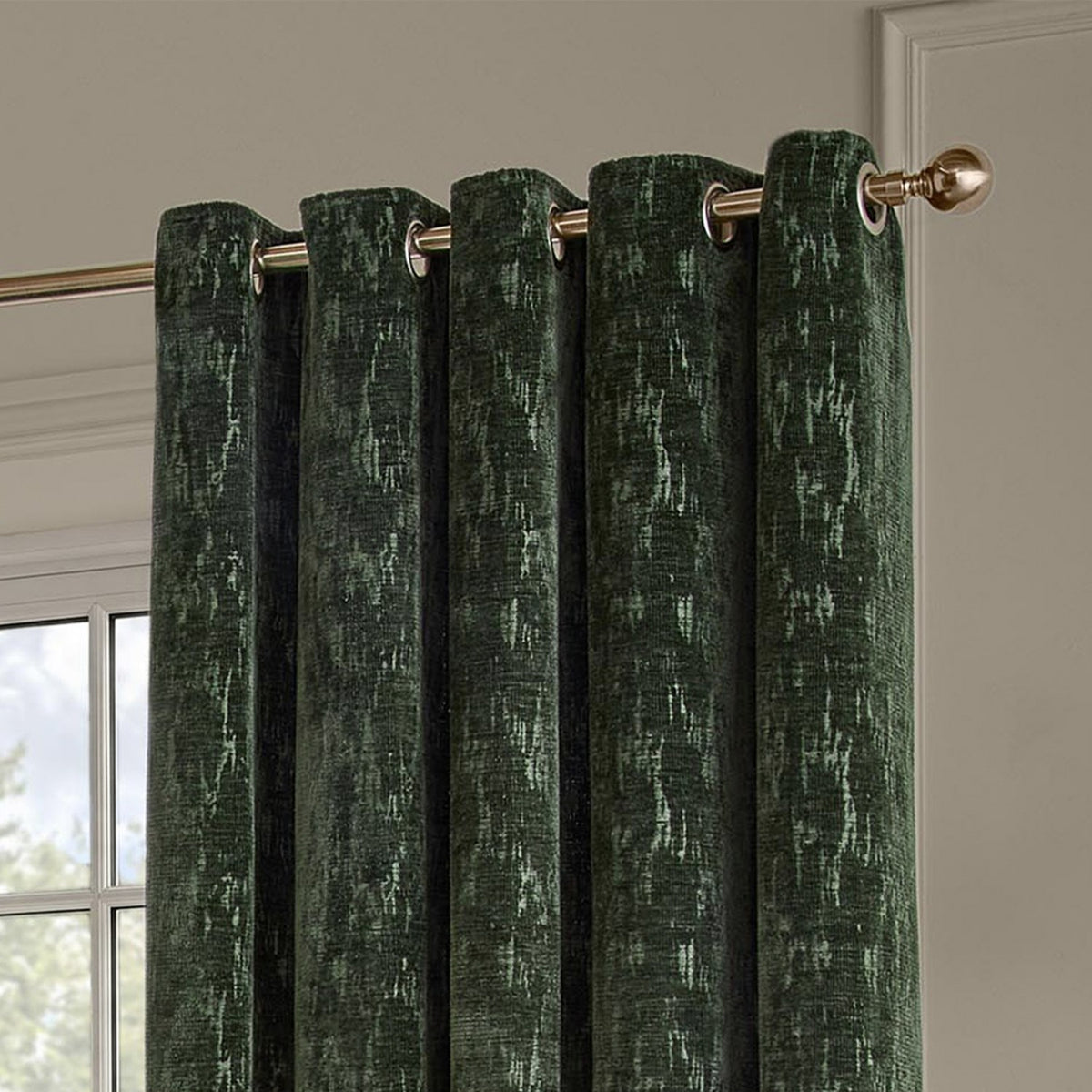 Aurelio Chenille Jacquard eyelet curtains in emerald green, showing brass eyelet rings on a gold curtain pole against a light neutral wall.
