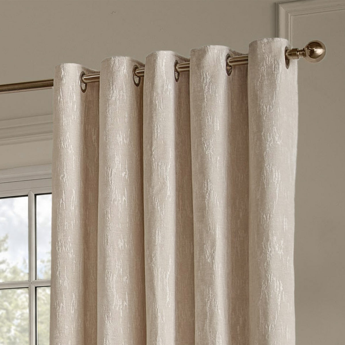 Aurelio Chenille Jacquard eyelet curtains in ivory, showing metal grommets on a bronze pole with woven abstract pattern, hung by a window.