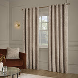 Aurelio Chenille Jacquard Eyelet Curtains in mink hung on a brass rod either side of a window, shown in a living room with a rust velvet armchair and matching cushion.