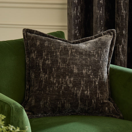 Aurelio Chenille Jacquard Polyester Cushion in charcoal with a flanged edge and abstract textured pattern, styled on a green velvet armchair.