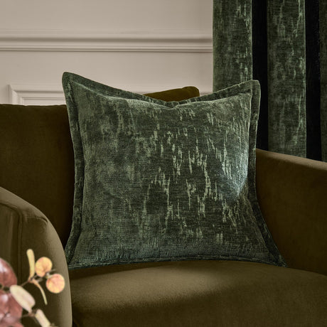 Aurelio Chenille Jacquard Polyester Cushion in emerald green with a flanged edge, showing a mottled woven texture, styled on an olive velvet sofa.