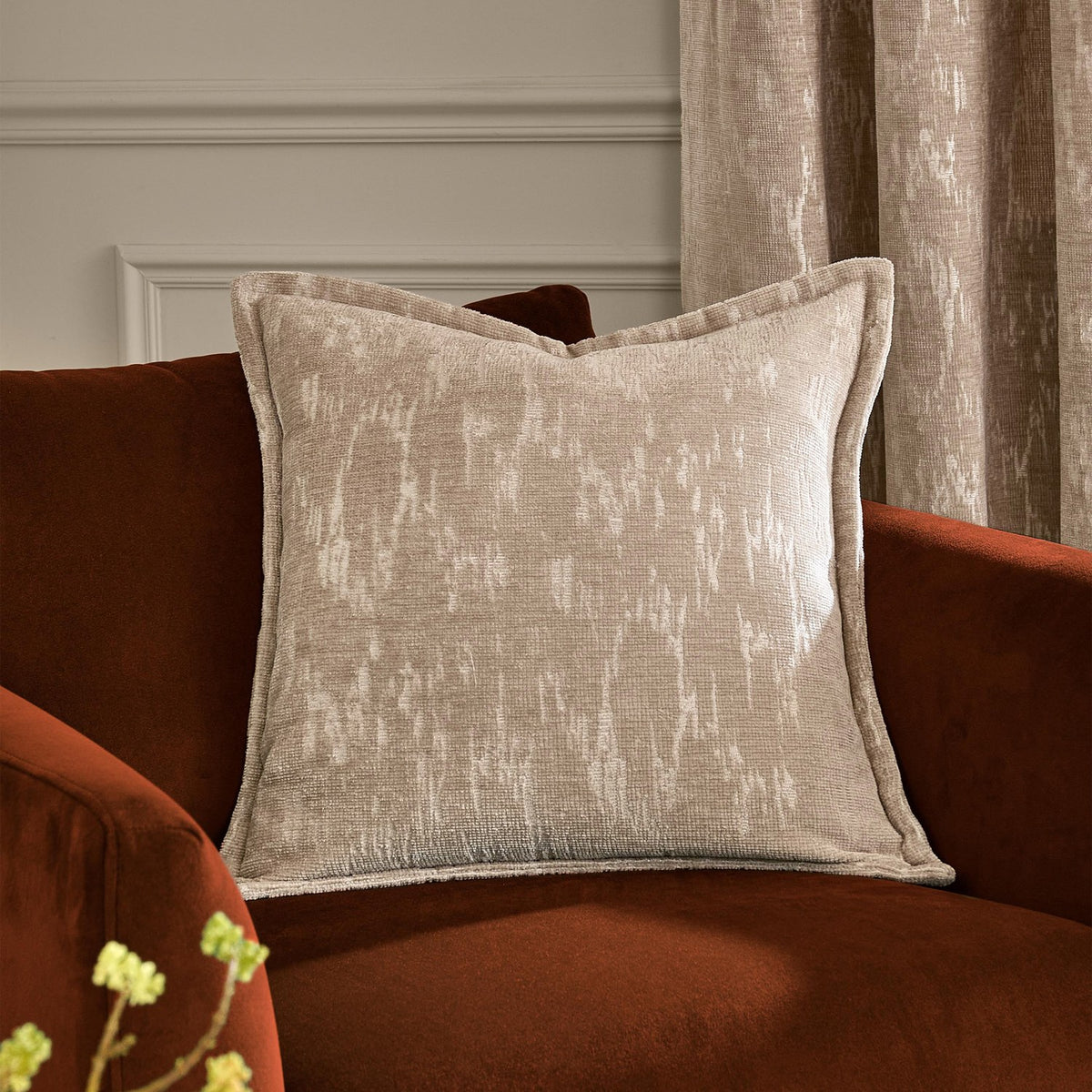 Aurelio Chenille Jacquard Polyester Cushion in mink beige with abstract jacquard pattern and flanged edge, styled on a rust velvet armchair near curtains.