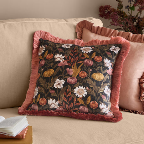 Autumn Garden Floral Velvet Cushion in Burnished Rose/Moss, square with pink fringed trim, on a beige sofa styled with pink cushions and books.