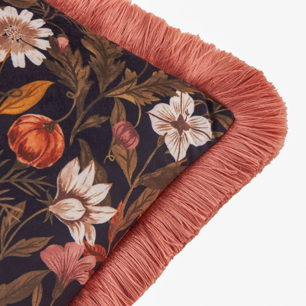 Autumn Garden Floral Velvet Cushion corner detail showing a dark floral print with rust pumpkins, cream blooms, and moss leaves, edged in burnished rose fringe.