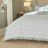 Ava Reversible Leaf Duvet Cover Set in White Sage dressed on a bed with sage green ruffled trim, shown in a bedroom setting with a lamp and side table.