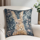 Avebury Animal Velvet Cushion in navy, square with a hare portrait in tan and amber tones amid pale florals, shown on a cream armchair.