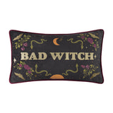 Rectangular velvet lumbar cushion in charcoal with burgundy piping, "Bad Witch" in gold embroidered lettering, surrounded by snakes, roses, bats and a crescent moon, on a white background.