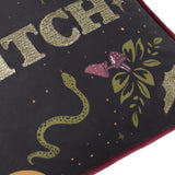 Close-up of the Bad Witch Embroidered Velvet Cushion in black, showing gold metallic lettering, a green snake, mushrooms and foliage design, with a burgundy velvet trim edge.