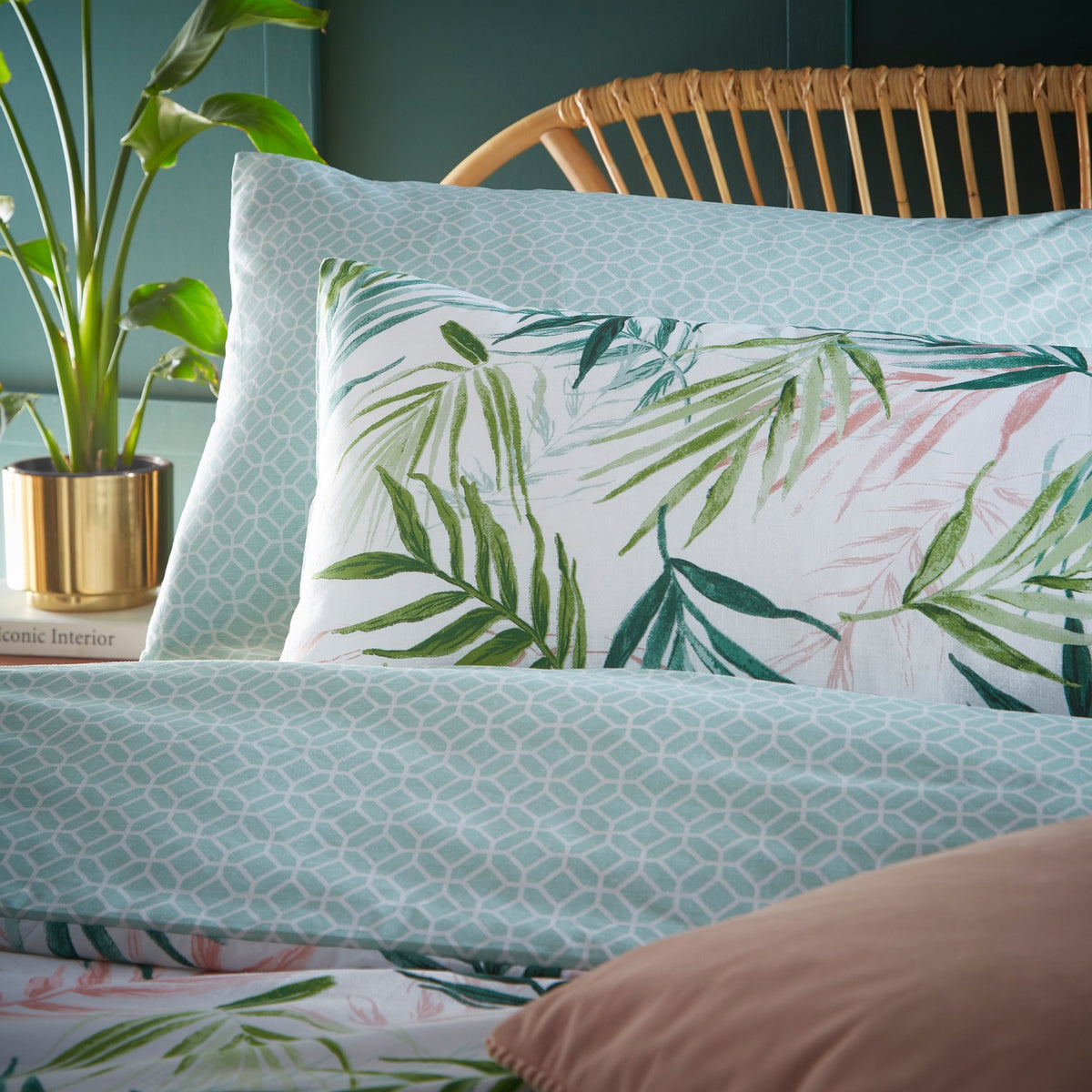 Bali Palm reversible duvet cover set styled on a bed, showing green palm leaf print pillowcases against a soft aqua geometric reverse, in a bedroom setting with rattan headboard and potted plant.