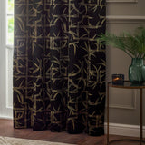 Bamboo Jacquard Lined Eyelet Curtain in black with pale gold bamboo cane and leaf pattern, shown hanging in a living room beside a green glass vase and side table.