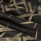 Close-up of black eyelet curtain fabric with jacquard-woven golden-tan bamboo canes and leaves in a loose geometric pattern, showing draped folds and subtle sheen.