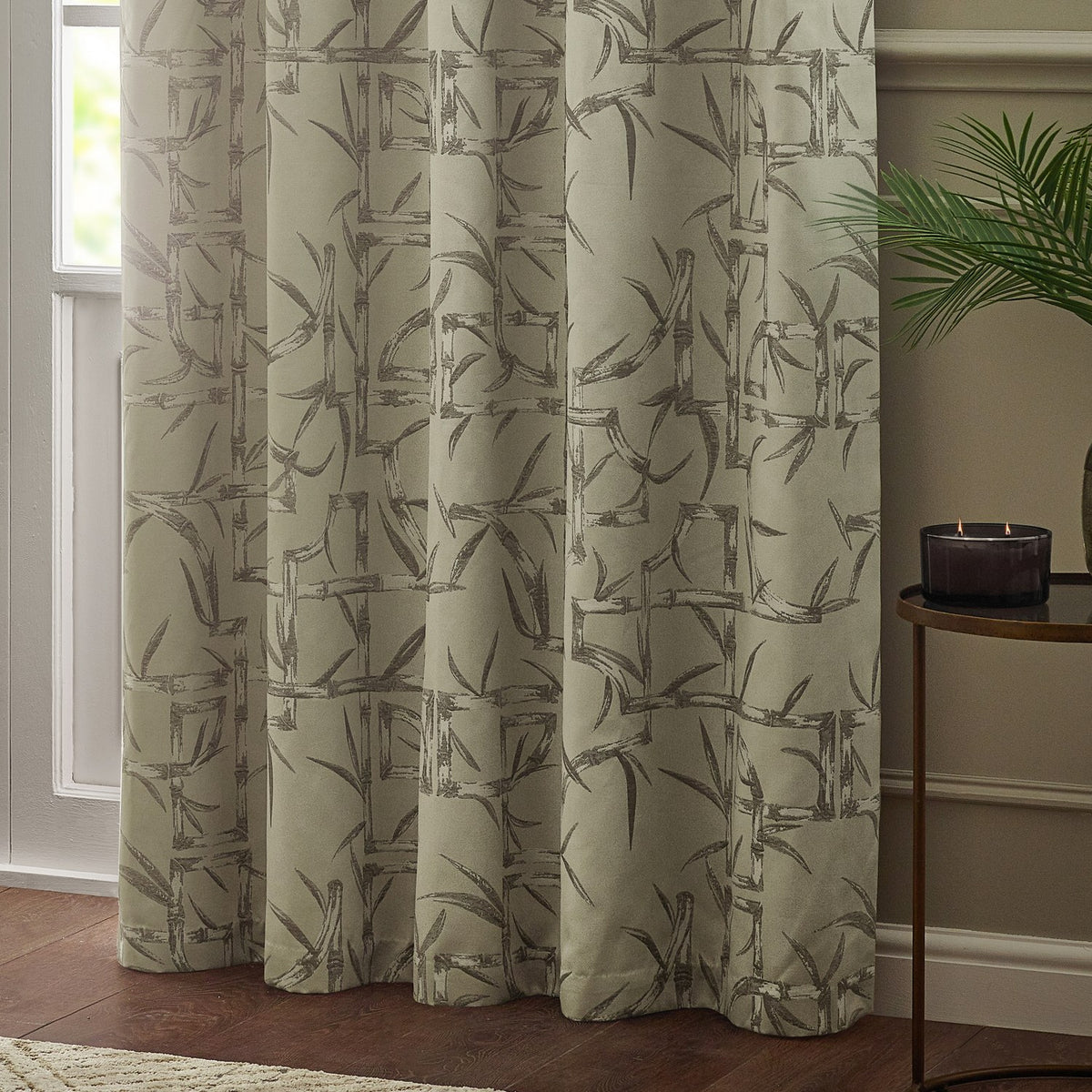 Bamboo Jacquard Lined Eyelet Curtains in champagne with grey bamboo pattern, hanging in a living room beside a window and side table.