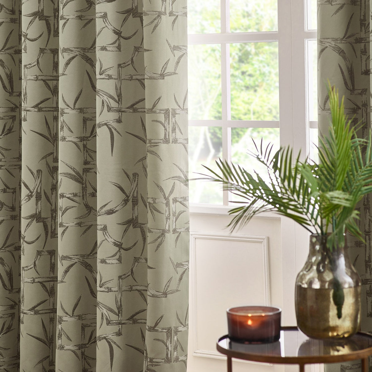 Bamboo Jacquard Lined Eyelet Curtains in champagne, showing the grey bamboo pattern on eyelet-topped drapes framing a window in a living room setting.