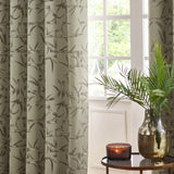 Bamboo Jacquard Lined Eyelet Curtains in champagne, showing the grey bamboo pattern on eyelet-topped drapes framing a window in a living room setting.