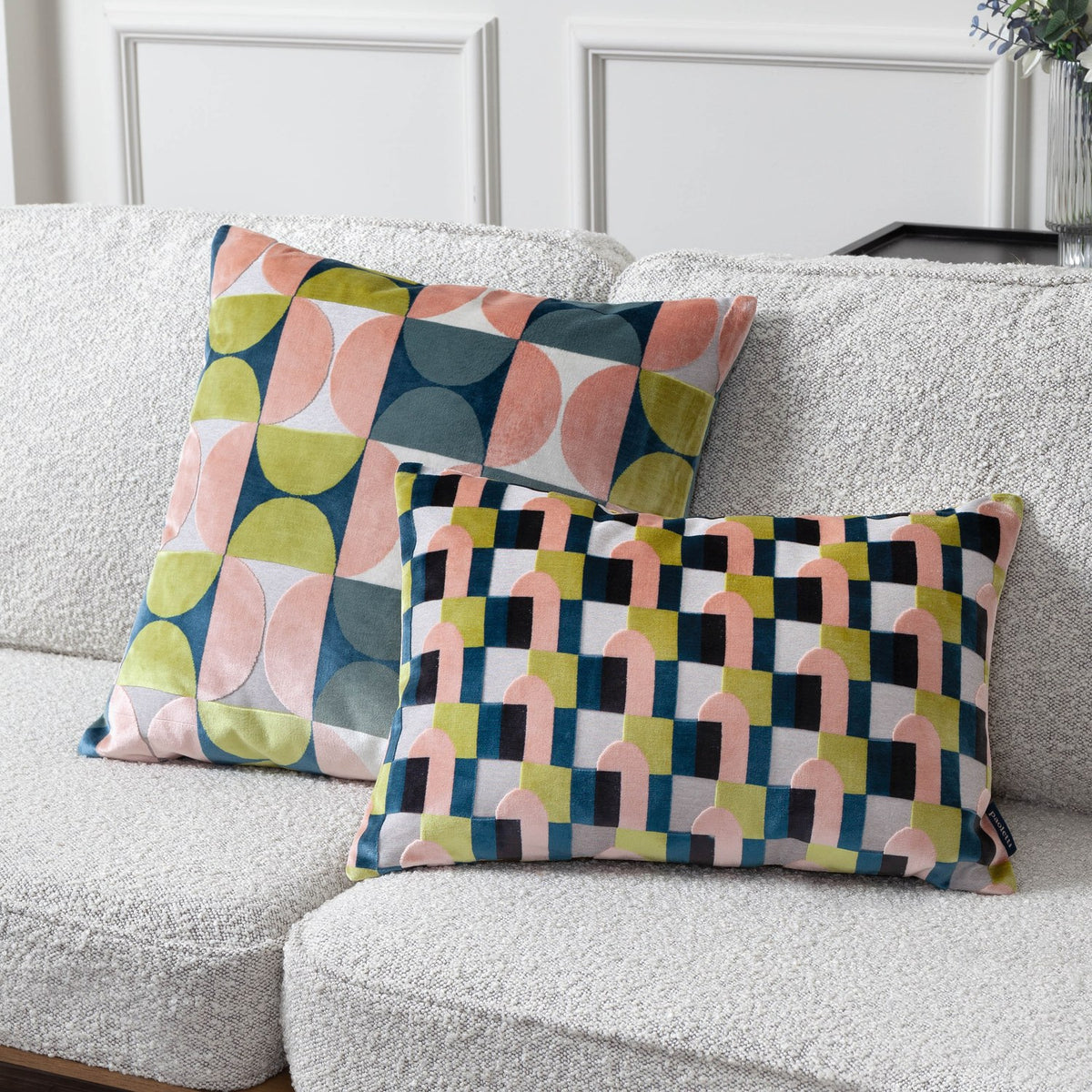 Two Bardot geometric cut-velvet cushions in pink, avocado green, navy and cream, one square and one rectangular, styled on a bouclé sofa.