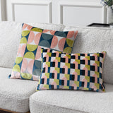 Two Bardot geometric cut-velvet cushions in pink, avocado green, navy and cream, one square and one rectangular, styled on a bouclé sofa.