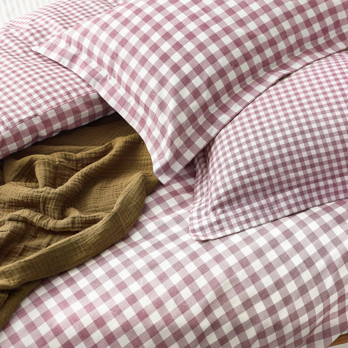 Barton Cotton Gingham Duvet Cover Set in Berry, showing pink and white checked pillowcases and duvet cover with a mustard textured throw folded on the bed.
