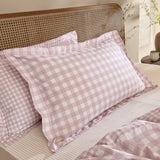 Barton Cotton Gingham Duvet Cover Set in blush, showing pink and white check pillow shams on a bed with a cane headboard and matching duvet corner visible.