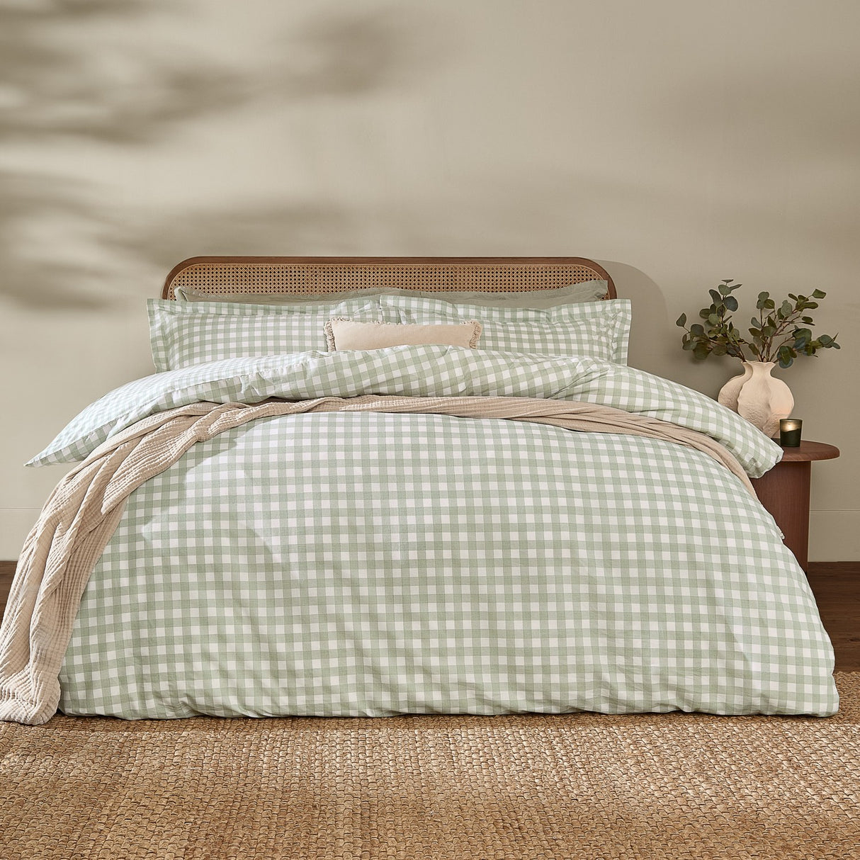 Barton Cotton Gingham Duvet Cover Set in eucalyptus green and white check, dressed on a bed with matching pillowcases in a bedroom with rattan headboard.