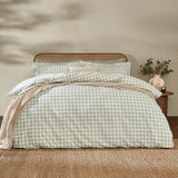 Barton Cotton Gingham Duvet Cover Set in eucalyptus green and white check, dressed on a bed with matching pillowcases in a bedroom with rattan headboard.