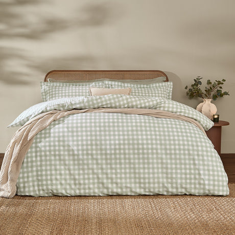 Barton Cotton Gingham Duvet Cover Set in eucalyptus green and white check, dressed on a bed with matching pillowcases in a bedroom with rattan headboard.