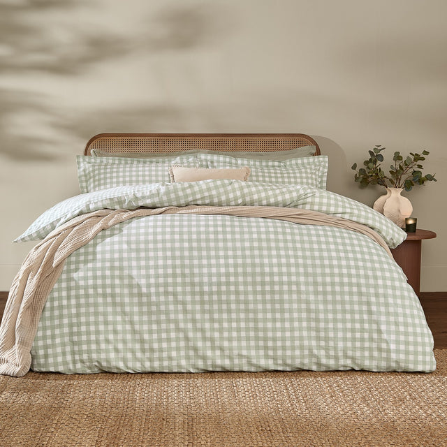 Barton Cotton Gingham Duvet Cover Set in eucalyptus green and white check, dressed on a bed with matching pillowcases in a bedroom with rattan headboard.