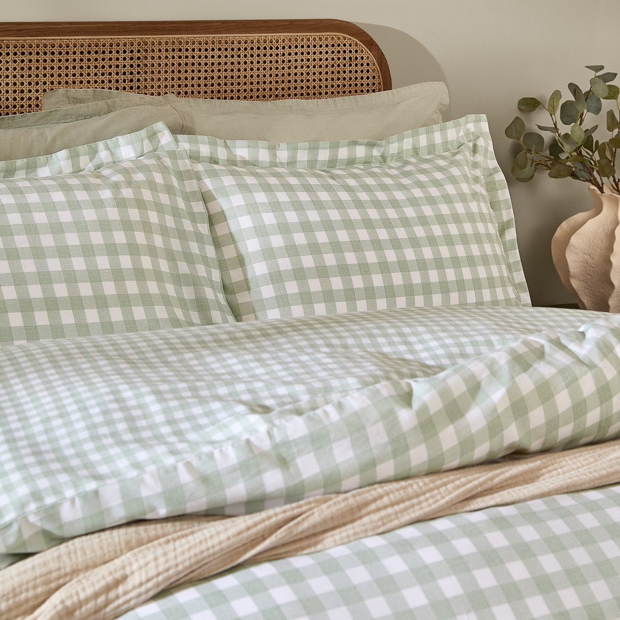 Barton Cotton Gingham Duvet Cover Set in Eucalyptus green and white check, styled on a bed with matching pillowcases against a rattan headboard.
