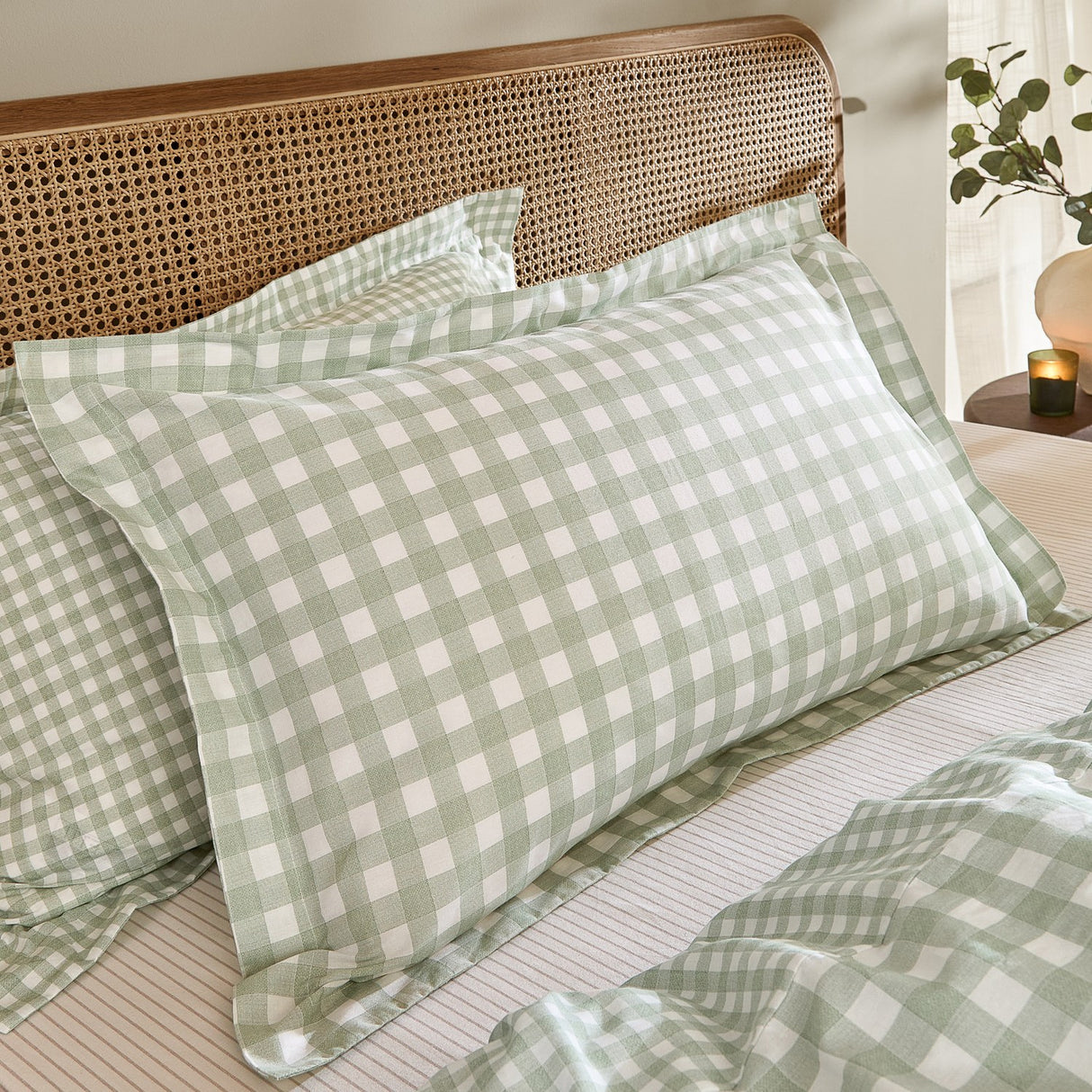 Barton Cotton Gingham Duvet Cover Set in Eucalyptus green and white check styled on a bed with pillow shams against a rattan headboard.