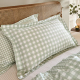 Barton Cotton Gingham Duvet Cover Set in Eucalyptus green and white check styled on a bed with pillow shams against a rattan headboard.