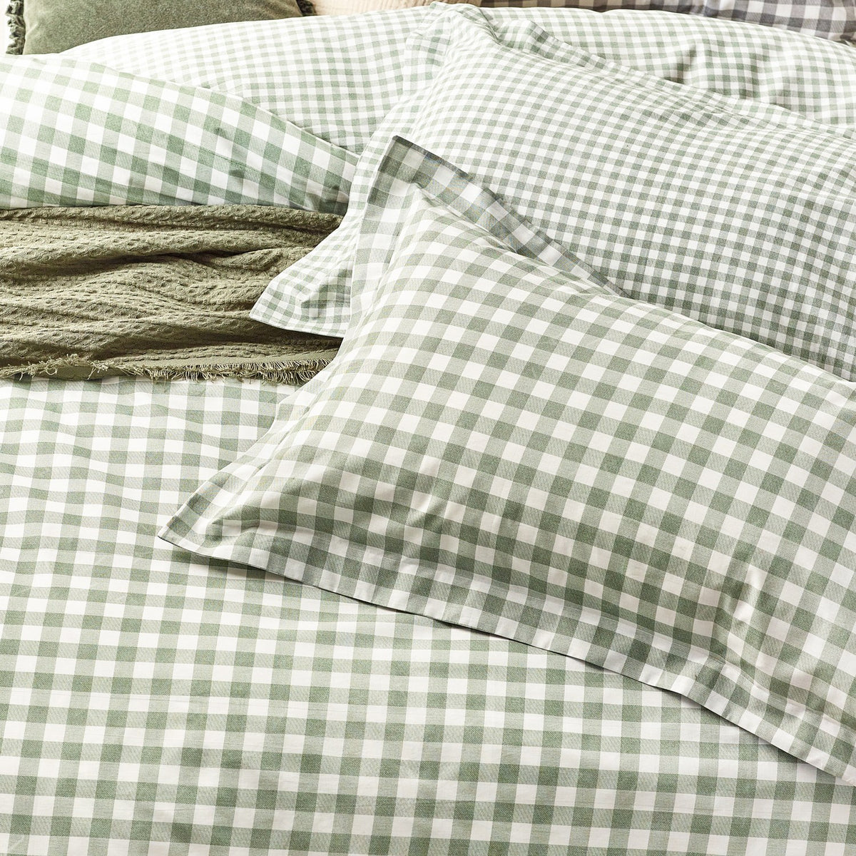 Barton Cotton Gingham Duvet Cover Set in Forest, showing green and white check pillowcases and duvet cover on a bed with a textured green throw folded alongside.