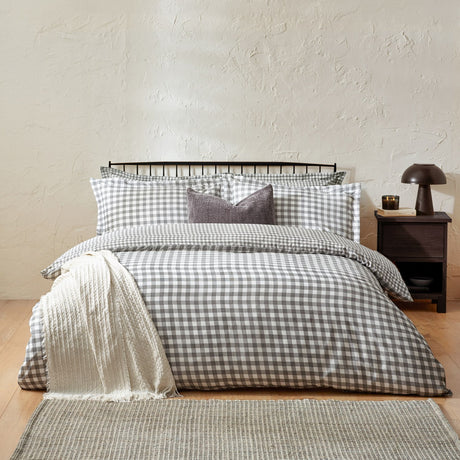 Barton Cotton Gingham Duvet Cover Set in grey and white check on a bed with matching pillowcases, a purple cushion, and a cream throw in a bedroom setting.