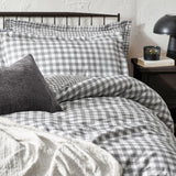 Barton Cotton Gingham Duvet Cover Set in grey and white, styled on a bed with matching pillowcases, a textured charcoal cushion, and a cream throw, in a bedroom setting.