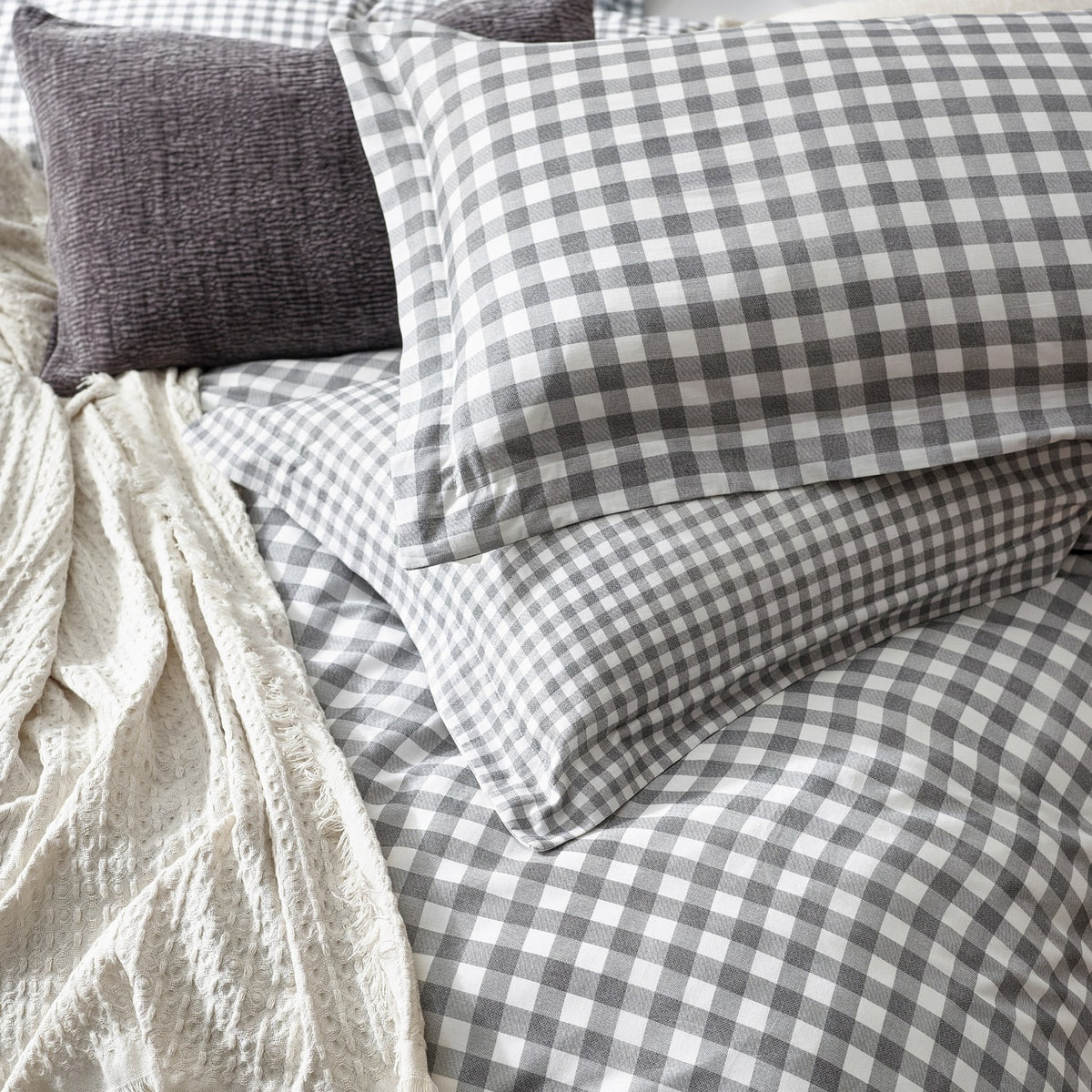 Barton Cotton Gingham Duvet Cover Set in Grey, showing reversible grey and white check pillowcases and duvet on a bed with a cream textured throw and dark cushion.