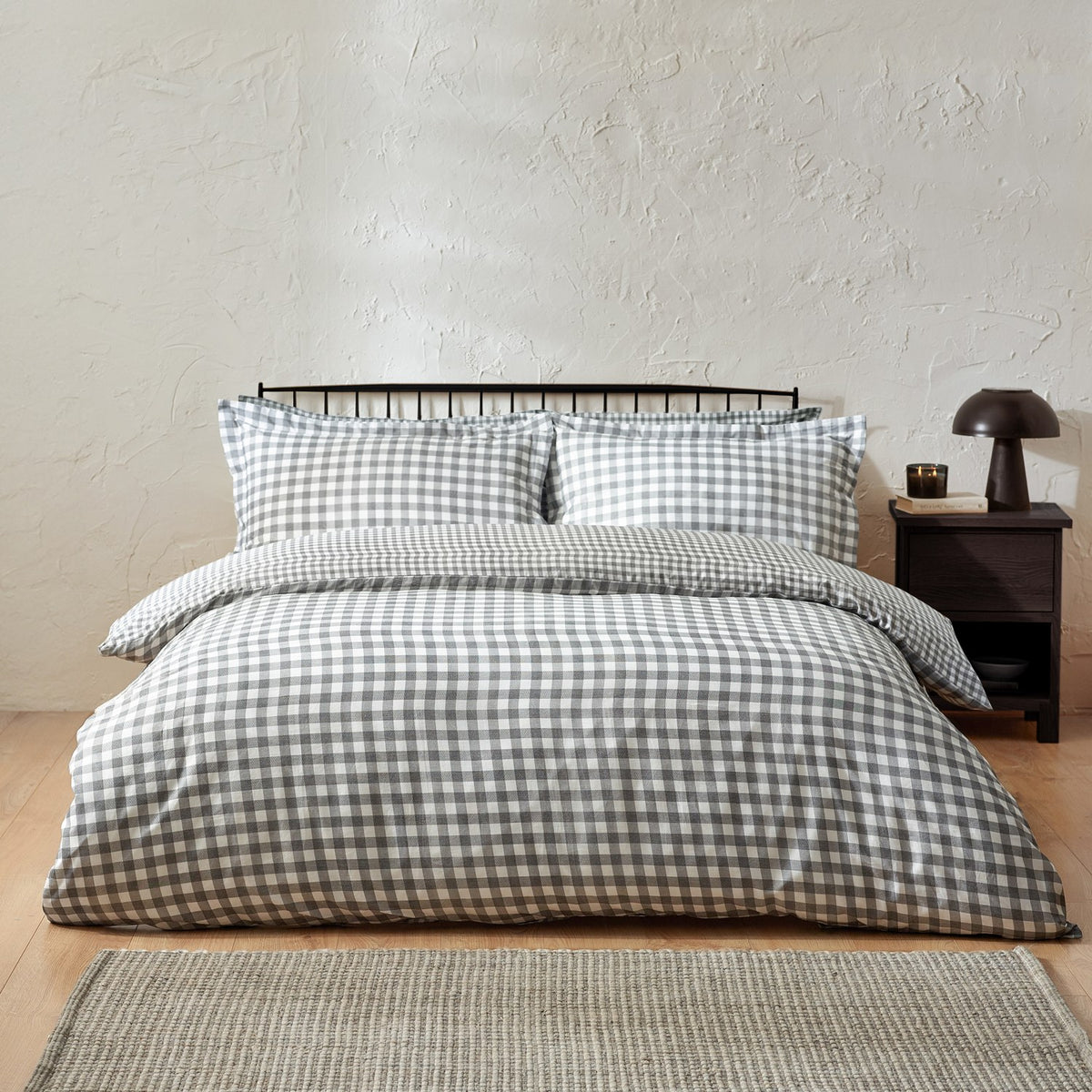 Barton Cotton Gingham Duvet Cover Set in Grey on a bed with matching pillowcases, shown in a bedroom with a dark headboard and bedside table.