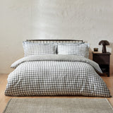 Barton Cotton Gingham Duvet Cover Set in Grey on a bed with matching pillowcases, shown in a bedroom with a dark headboard and bedside table.