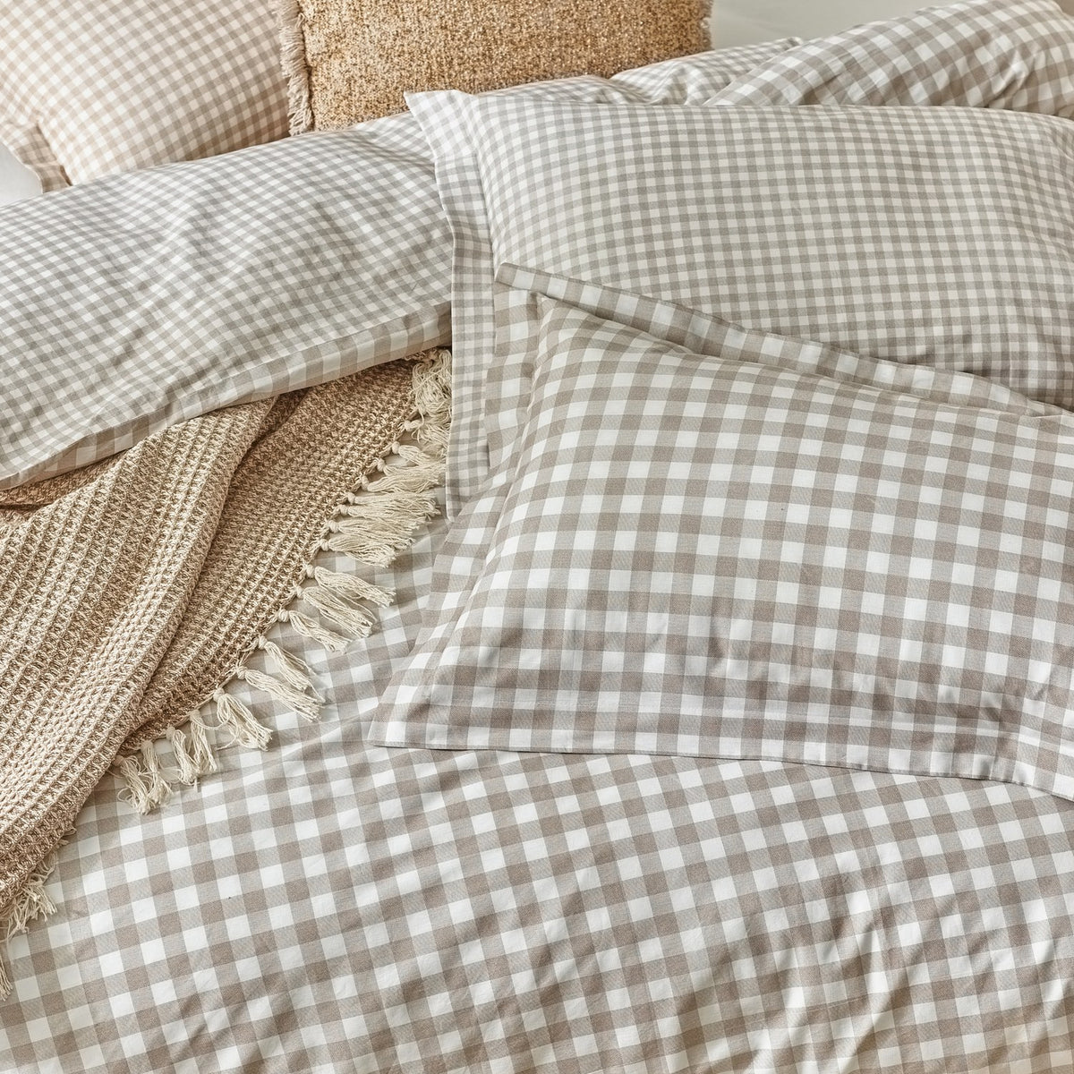 Barton Cotton Gingham Duvet Cover Set in Natural, showing pillowcases and duvet in a beige-and-white check on a bed with a waffle-knit fringed throw and textured cushion.