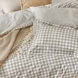Barton Cotton Gingham Duvet Cover Set in Natural, showing pillowcases and duvet in a beige-and-white check on a bed with a waffle-knit fringed throw and textured cushion.