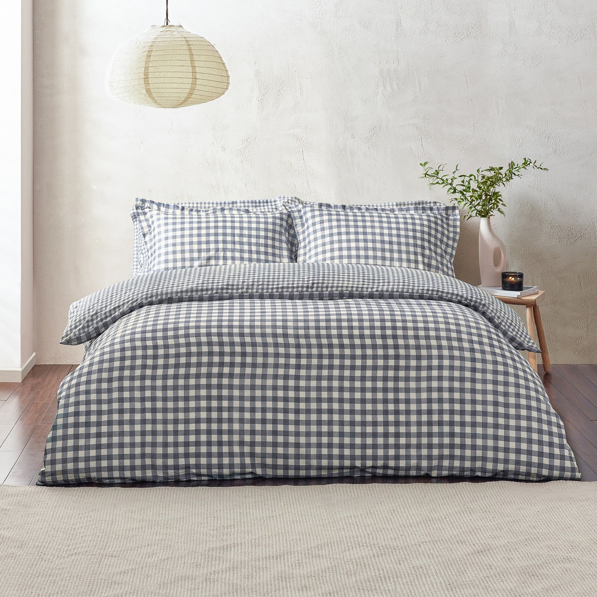 Barton Cotton Gingham Duvet Cover Set in Navy dressed on a bed with matching pillowcases, shown in a bedroom with a paper pendant light and wooden side table.