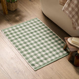 Barton Gingham Cotton Bath Mat in forest green and cream check, shown on a wooden bathroom floor beside a bathtub and wooden stool with soap.