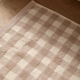 Barton Gingham Cotton Bath Mat in natural, showing woven taupe and cream check pattern with looped cotton pile, corner folded back on a wooden floor.